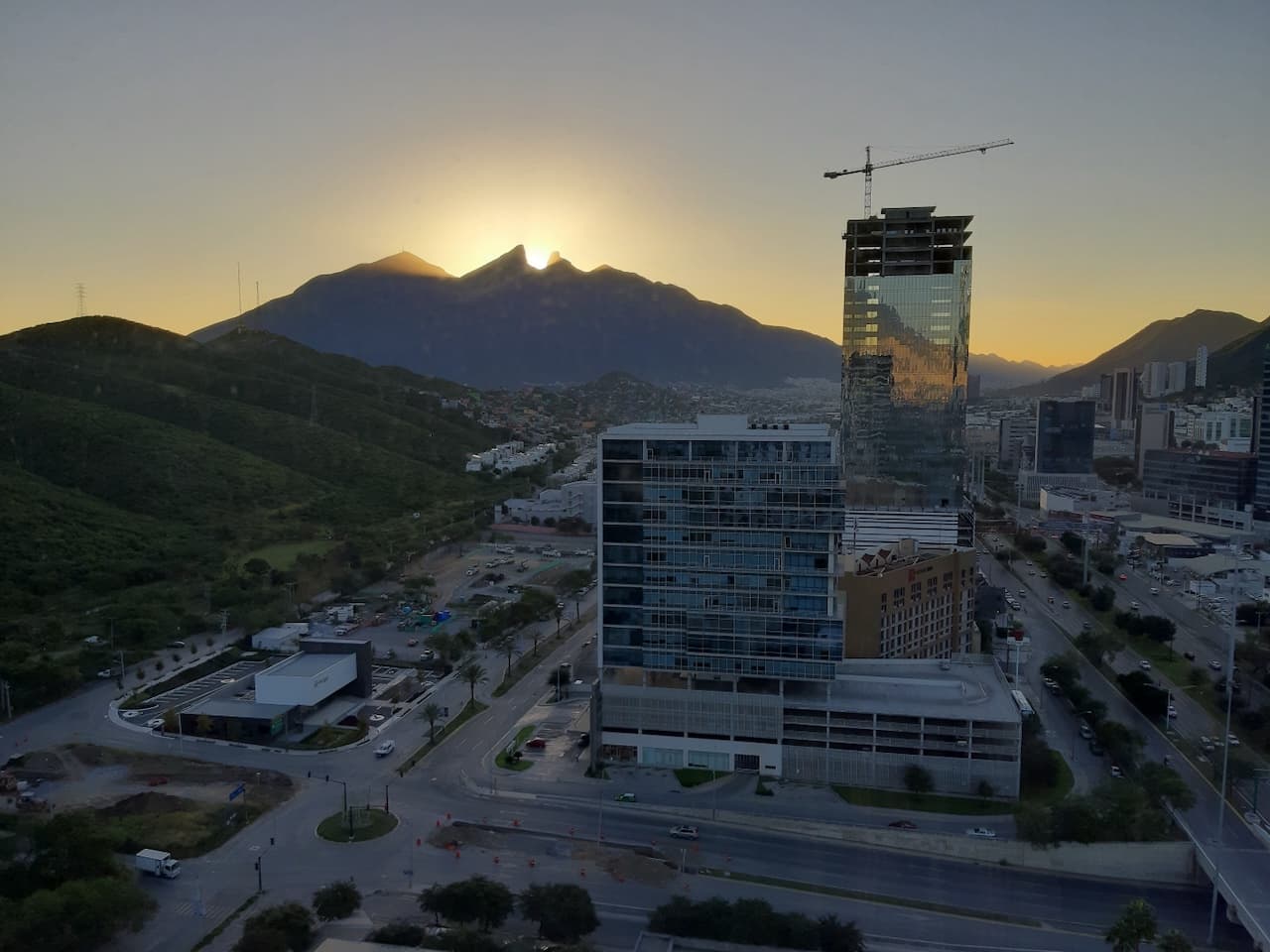 Vista panorámica de una ciudad al atardecer, con montañas al fondo y edificios modernos en primer plano.