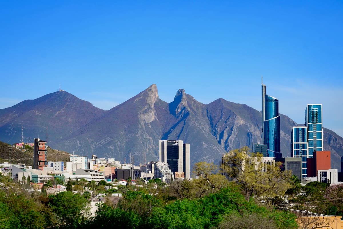 Vista panorámica de la ciudad con edificios modernos al frente y montañas al fondo, bajo un cielo despejado.