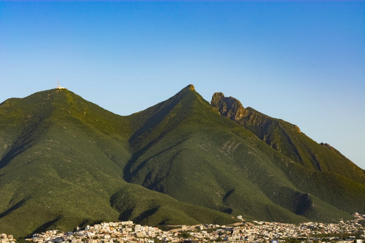 Montañas verdes al fondo con un cielo despejado y una ciudad al pie de las colinas.